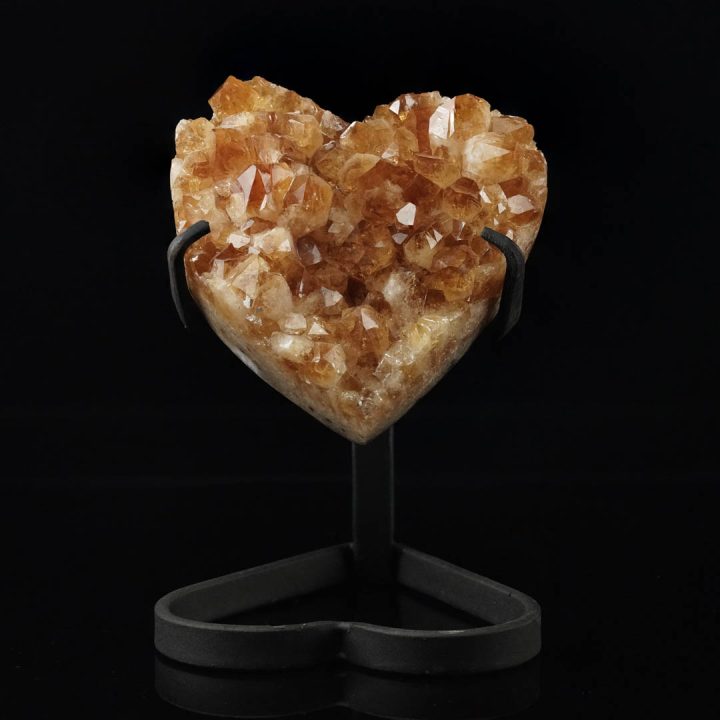 Citrine crystal heart displayed on metal stand against black background