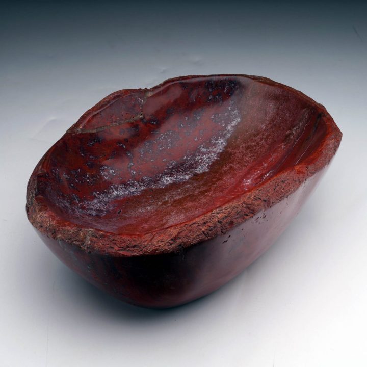 Fossilized red petrified wood bowl showcasing layered natural color variation and organic stone form