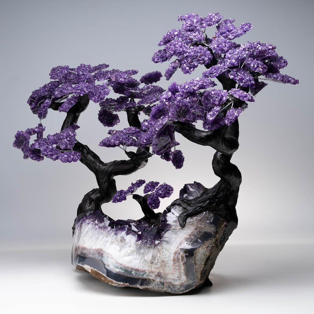 A striking sculpture of a bonsai tree with dark branches and vibrant purple amethyst crystal leaves, rooted in a geode.
