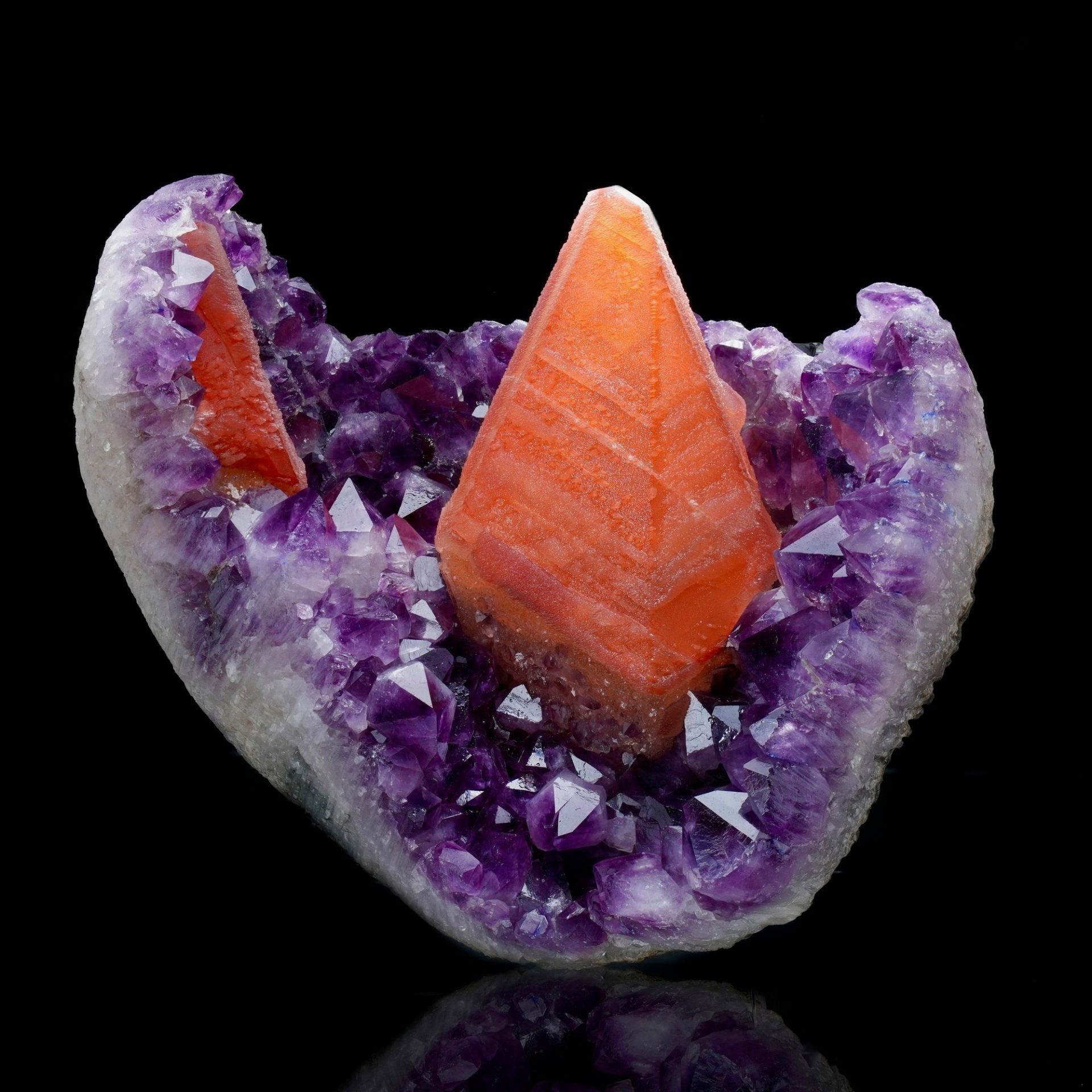 A vibrant amethyst geode with shimmering purple crystals, encasing a prominent orange pyramid-shaped mineral specimen.