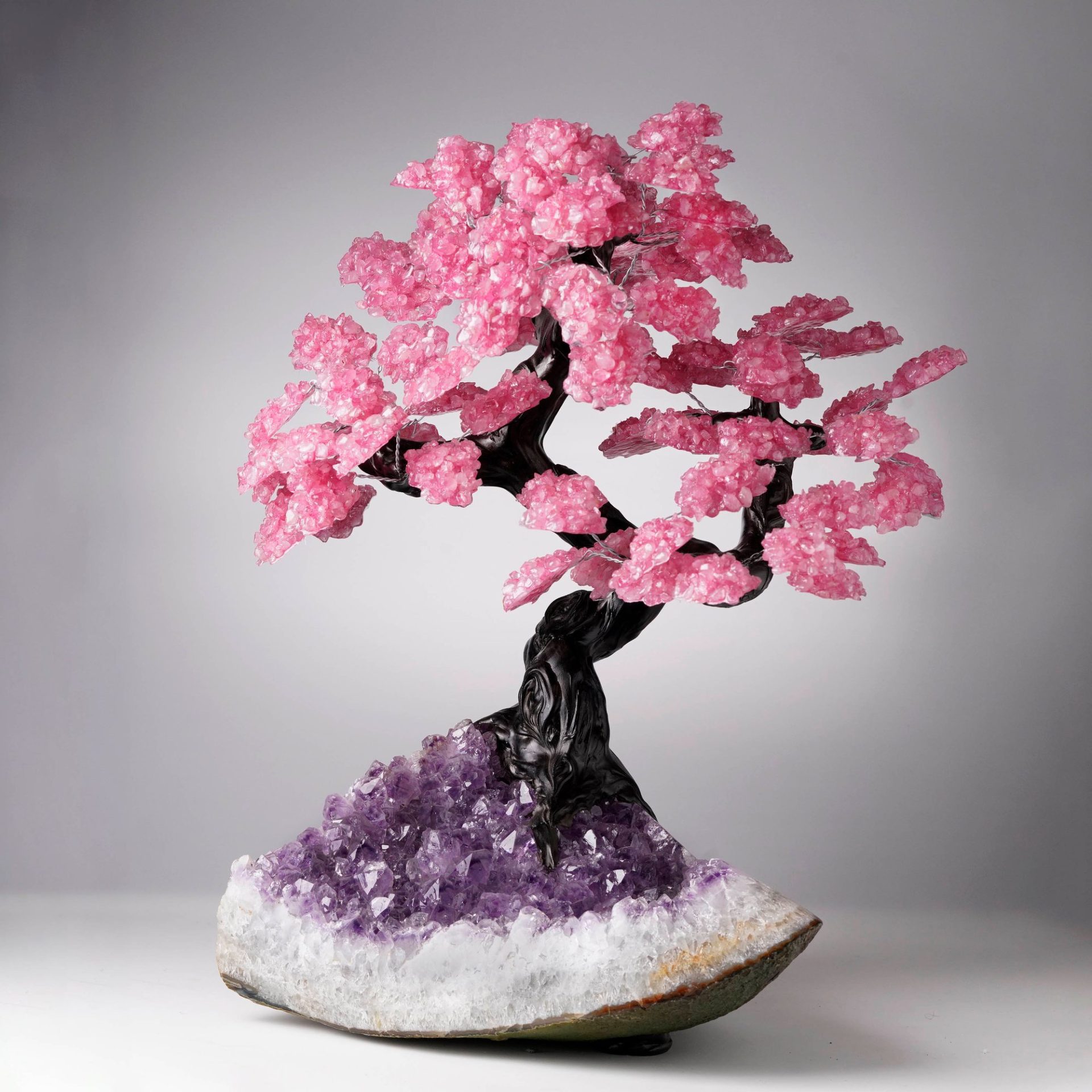 A unique bonsai tree art piece with pink crystal flowers emerging from a purple amethyst geode.