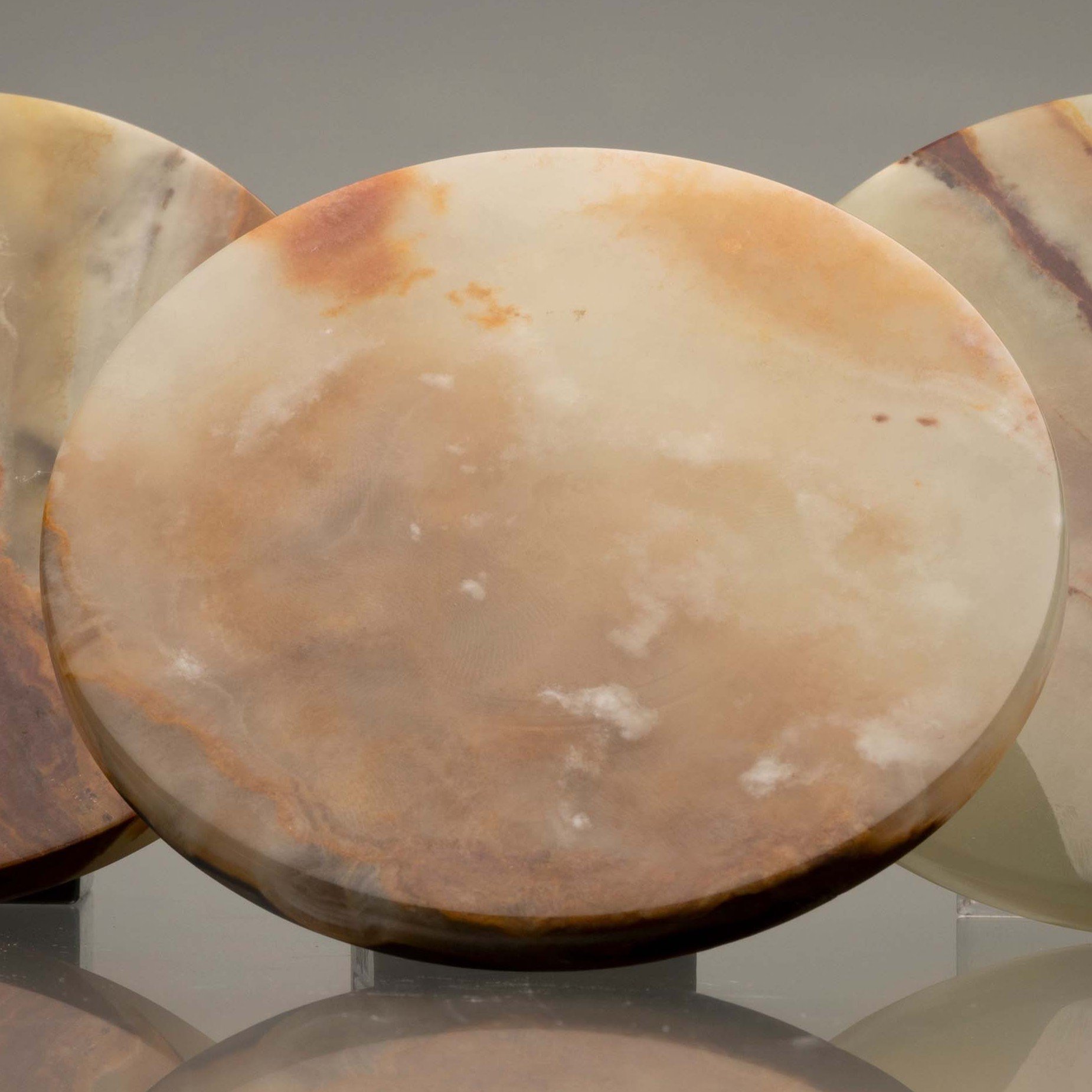 Three round, polished stone objects, possibly onyx, with natural cream and brown patterns on a reflective surface.