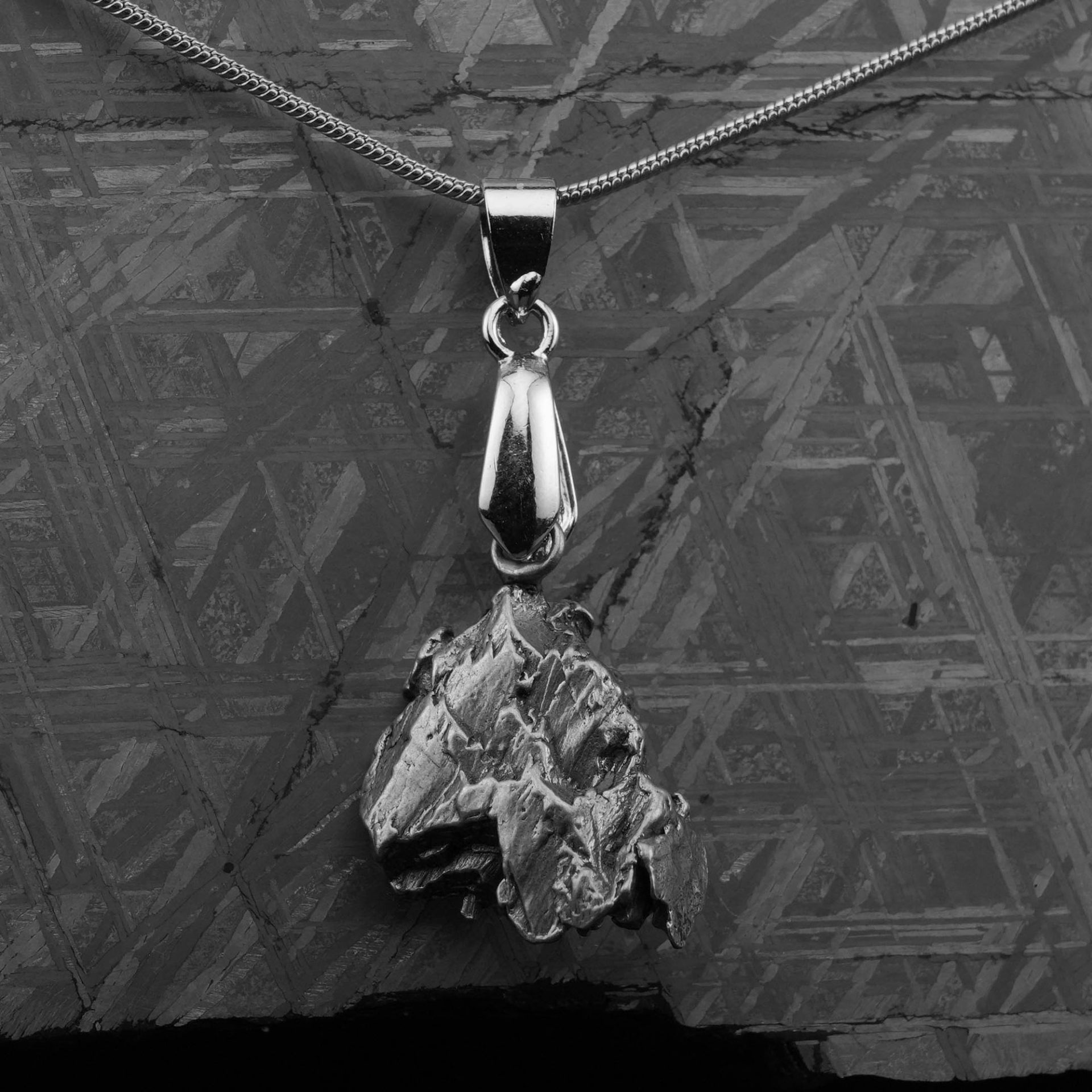 A silver necklace with a rough metallic pendant hangs over a textured meteorite slab.